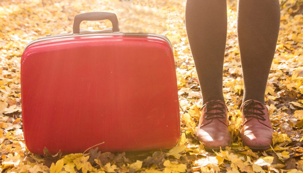 een rode koffer met de benen en schoenen van een vrouw